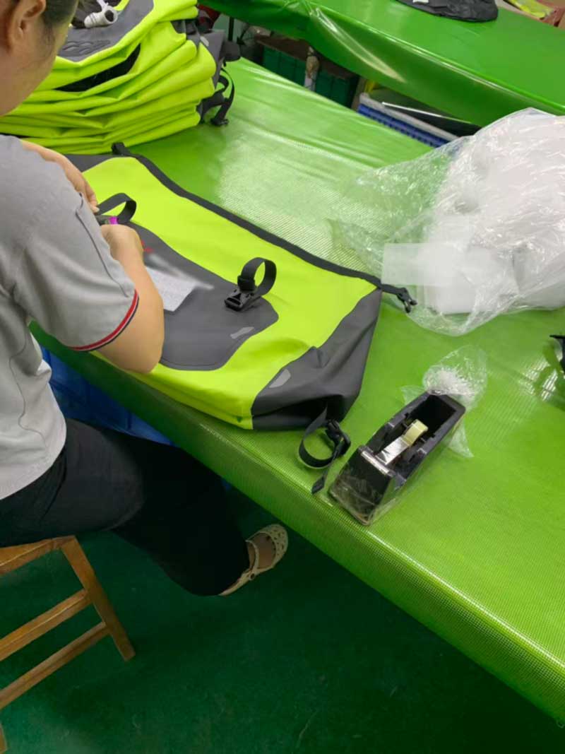 Worker fitting webbing straps and buckles to a waterproof motorcycle bag with accessory pack alongside